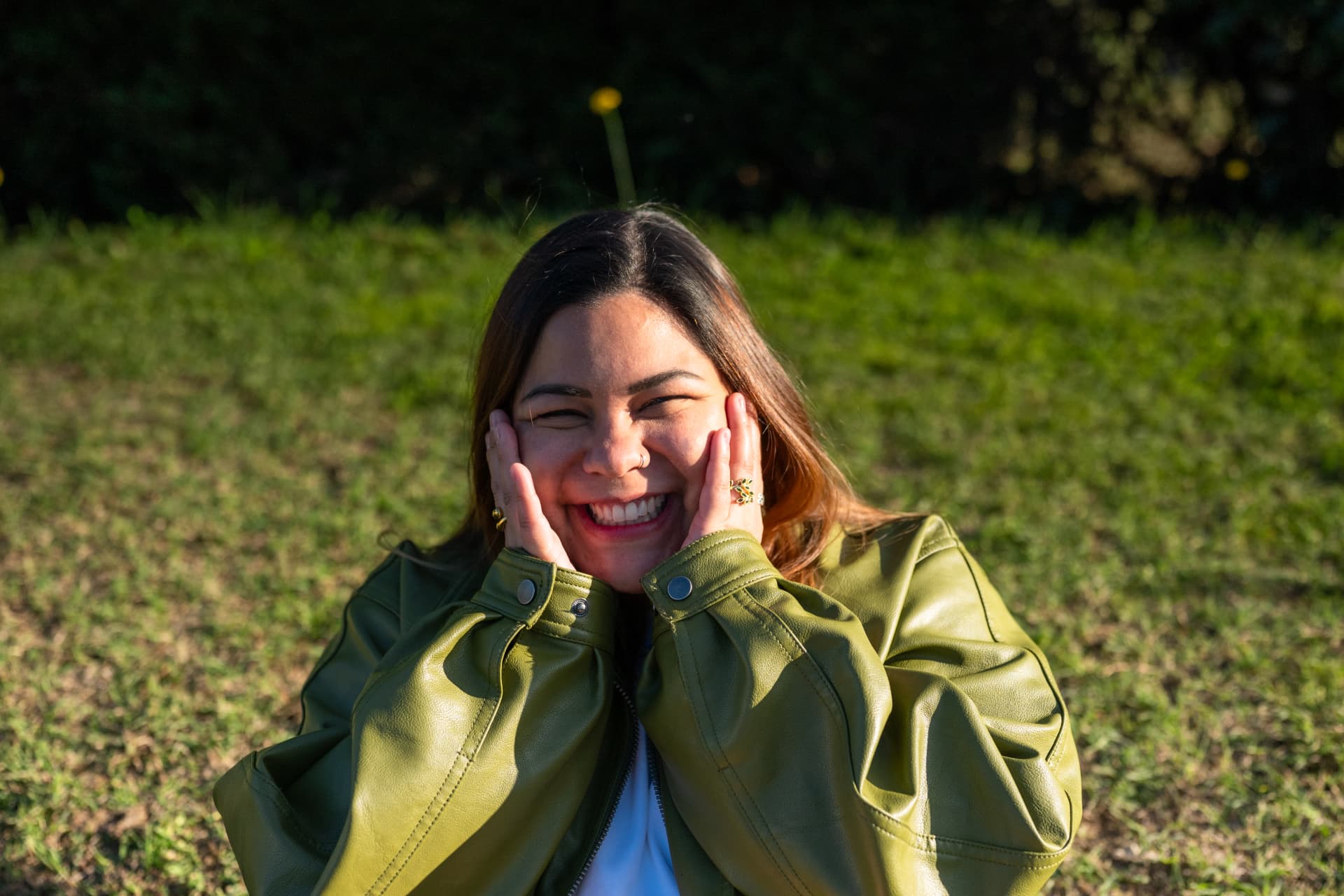 Dayanna laughing in a green jacket, sitting on the grass